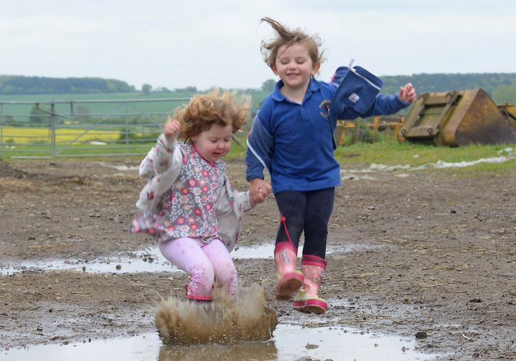 children jumping in muddy puddle in farmyard